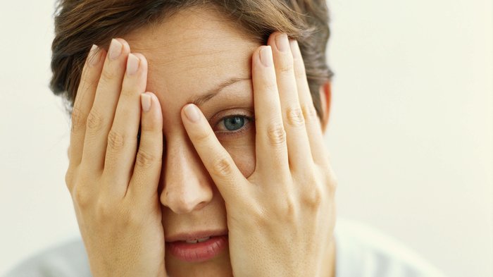 anxious woman peeking between her fingers with both hands on her face
