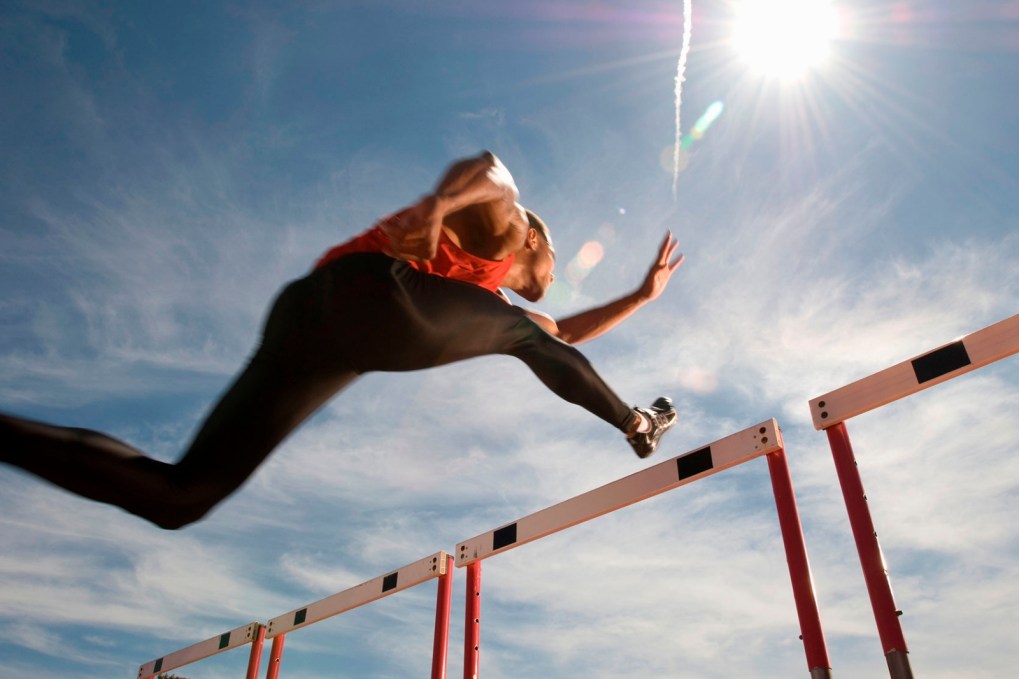 person jumping over a hurdle with the sunny sky in the background