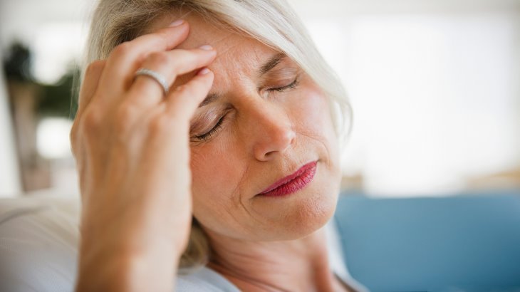 Face of a woman with white hair with a hand on her forehead and eyes closed