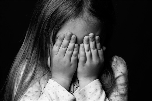 little girl with hands over her face in black and white