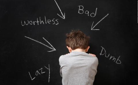 back of a child's head and torso with a chalkboard behind them listing negative words and arrows pointing to the child