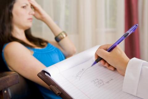 woman in blue shirt behind a notebook with an arm holding a pen