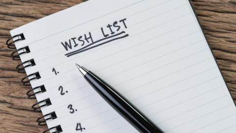 a white spiral notebook with a brown wooden background, on the page it has WISH LIST underlined twice and lines numbered 1 through 4