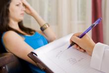 woman in blue shirt behind a notebook with an arm holding a pen